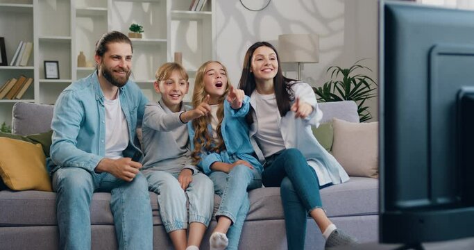 Happy man and woman relaxing with daughter and son watching television at home together. Cheerful family relaxing on sofa at home watching movie with children.