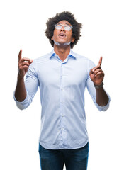 Afro american business man wearing glasses over isolated background amazed and surprised looking up and pointing with fingers and raised arms.