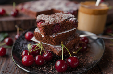 Chocolate cake with cherries on a black plate on wooden table