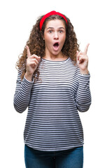 Beautiful brunette curly hair young girl wearing stripes sweater over isolated background amazed and surprised looking up and pointing with fingers and raised arms.