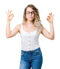 Beautiful young blonde woman wearing glasses over isolated background relax and smiling with eyes closed doing meditation gesture with fingers. Yoga concept.