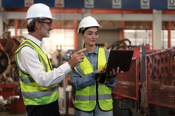 Industrial engineer and colleague wear safety helmets examining production in heavy metal engineering factories. Beard man industry inspector inspecting metalwork in manufacturing warehouse facility.