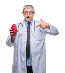 Handsome senior cardiologist doctor man holding heart over isolated background with surprise face pointing finger to himself