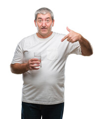 Handsome senior man drinking glass of water over isolated background with surprise face pointing finger to himself
