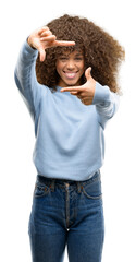 African american woman wearing a sweater smiling making frame with hands and fingers with happy face. Creativity and photography concept.