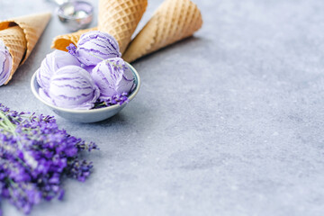 Berry ice cream scoops in a bowl with lavender flowers and waffle cones on a gray background. Summer healthy dessert. Space for text. selective focus