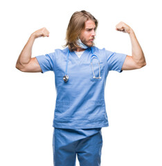 Young handsome doctor man with long hair over isolated background showing arms muscles smiling proud. Fitness concept.