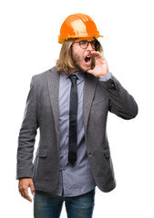 Young handsome architec man with long hair wearing safety helmet over isolated background shouting and screaming loud to side with hand on mouth. Communication concept.