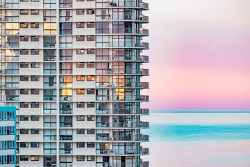 Close up section of high rise seaside apartment building with pink sunset over the beach on the...