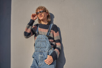 Blonde curly man in perfect look and stylish glasses posing in relaxed pose to the camera