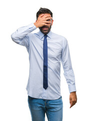 Adult hispanic business man over isolated background peeking in shock covering face and eyes with hand, looking through fingers with embarrassed expression.