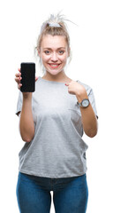 Young blonde woman showing screen of smartphone over isolated background with surprise face pointing finger to himself