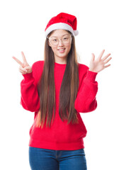 Fototapeta na wymiar Young Chinese woman over isolated background wearing christmas hat showing and pointing up with fingers number seven while smiling confident and happy.
