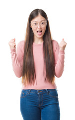 Young Chinese woman over isolated background wearing glasses celebrating surprised and amazed for success with arms raised and open eyes. Winner concept.