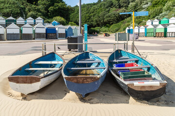 Three rowboats on the beach in front of beach huts at Middle Chine, Bournemouth, UK  