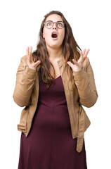 Beautiful plus size young woman wearing a dress and leather jacket over isolated background crazy and mad shouting and yelling with aggressive expression and arms raised. Frustration concept.