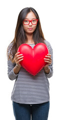 Young asian woman in love holding read heart over isolated background with a confident expression on smart face thinking serious