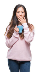 Young asian woman drinking coffee over isolated background cover mouth with hand shocked with shame for mistake, expression of fear, scared in silence, secret concept