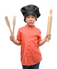 Fototapeta premium Dark haired little child wearing chef uniform with a confident expression on smart face thinking serious