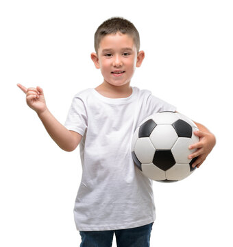 Dark haired little child playing with soccer ball very happy pointing with hand and finger to the side