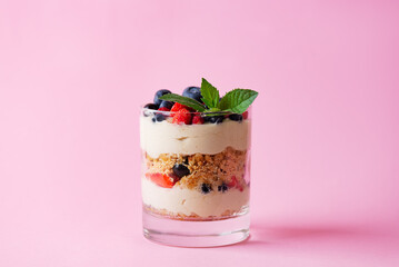 Sweet dessert in a glass with berries, mint, whipped cream and biscuit on a pink background. Healthy food, vegan, sugar, gluten and lactose free.