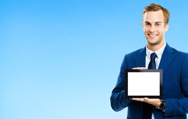 Portrait of businessman showing blank tablet pc, with copy space area for some text, advertising or slogan, over blue background. Smiling man at business studio concept.