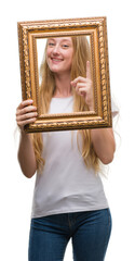 Blonde teenager woman holding vintage frame art surprised with an idea or question pointing finger with happy face, number one