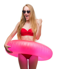 Blonde teenager woman wearing bikini and holding pink floater screaming proud and celebrating...
