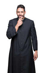 Young Christian priest over isolated background looking confident at the camera with smile with crossed arms and hand raised on chin. Thinking positive.
