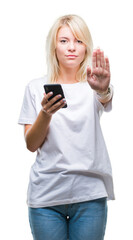 Fototapeta premium Young beautiful blonde woman using smartphone over isolated background with open hand doing stop sign with serious and confident expression, defense gesture