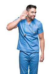 Handsome young doctor surgeon man over isolated background smiling with hand over ear listening an hearing to rumor or gossip. Deafness concept.