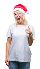 Young beautiful blonde woman wearing christmas hat over isolated background doing happy thumbs up gesture with hand. Approving expression looking at the camera with showing success.