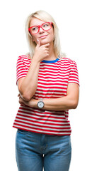 Young beautiful blonde woman wearing glasses over isolated background with hand on chin thinking about question, pensive expression. Smiling with thoughtful face. Doubt concept.