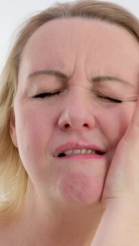 vertical video. Young caucasian woman touch her cheek having severe toothache sitting on couch at home, unhealthy brunette girl 20s suffers from painful sensations need dental service, medical