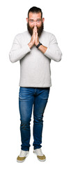 Young blond man wearing casual sweater praying with hands together asking for forgiveness smiling confident.