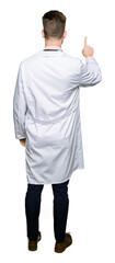 Young handsome doctor man wearing medical coat Posing backwards pointing behind with finger hand