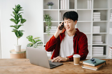Young attractive Asian man smiling thinking planning writing in notebook, tablet and laptop working from home  at home office