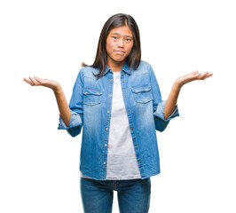 Young asian woman over isolated background clueless and confused expression with arms and hands raised. Doubt concept.