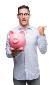 Handsome young man holding a piggy bank pointing with hand and finger up with happy face smiling