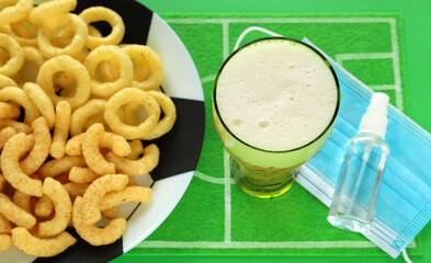 Puffed corn snacks on soccer ball plate, focus on top of beer glass, green football field dish mat....