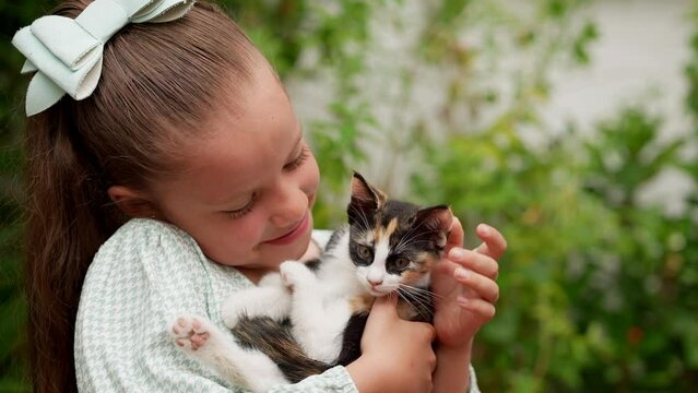 Niña linda latina rubia feliz con una gran sonrisa acariciando jugando con mascota un pequeño gatito gato felino travieso e inquieto y curioso en el jardín al exterior al aire libre un día lluvioso 