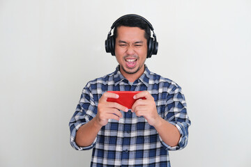 Adult Asian man wearing headphones showing excited expression when playing mobile games