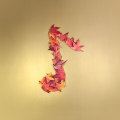 Music note made of red and yellow autumn leaves against gold background. Minimal concept. Copy space. Fall art. Creative autumn design. Music.