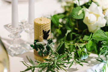 Festive table decorated with a composition of white flowers and greenery, and candles in the banquet hall. Table newlyweds covered with a tablecloth in the banquet area on a wedding party. Closeup.