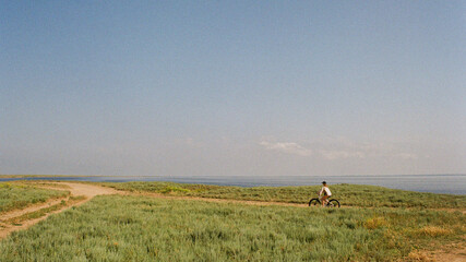 A person riding a bike in summer through a field next to a sea 