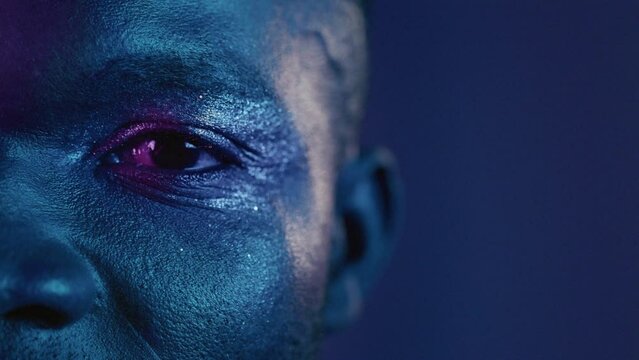 Close up portrait of a beautiful African American man in the studio. Attractive millennial gay guy opens eyes, neon blue pink light. Professional male transsexual model. Art make up, beauty fashion