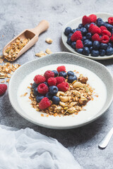 Granola with yogurt, raspberries, blueberries in a plate on a gray background