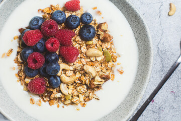 Granola with yogurt, raspberries, blueberries in a plate on a gray background