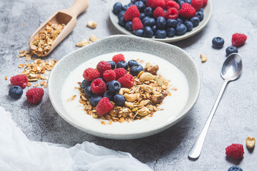 Granola with yogurt, raspberries, blueberries in a plate on a gray background