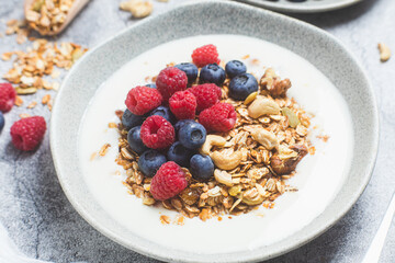 Granola with yogurt, raspberries, blueberries in a plate on a gray background